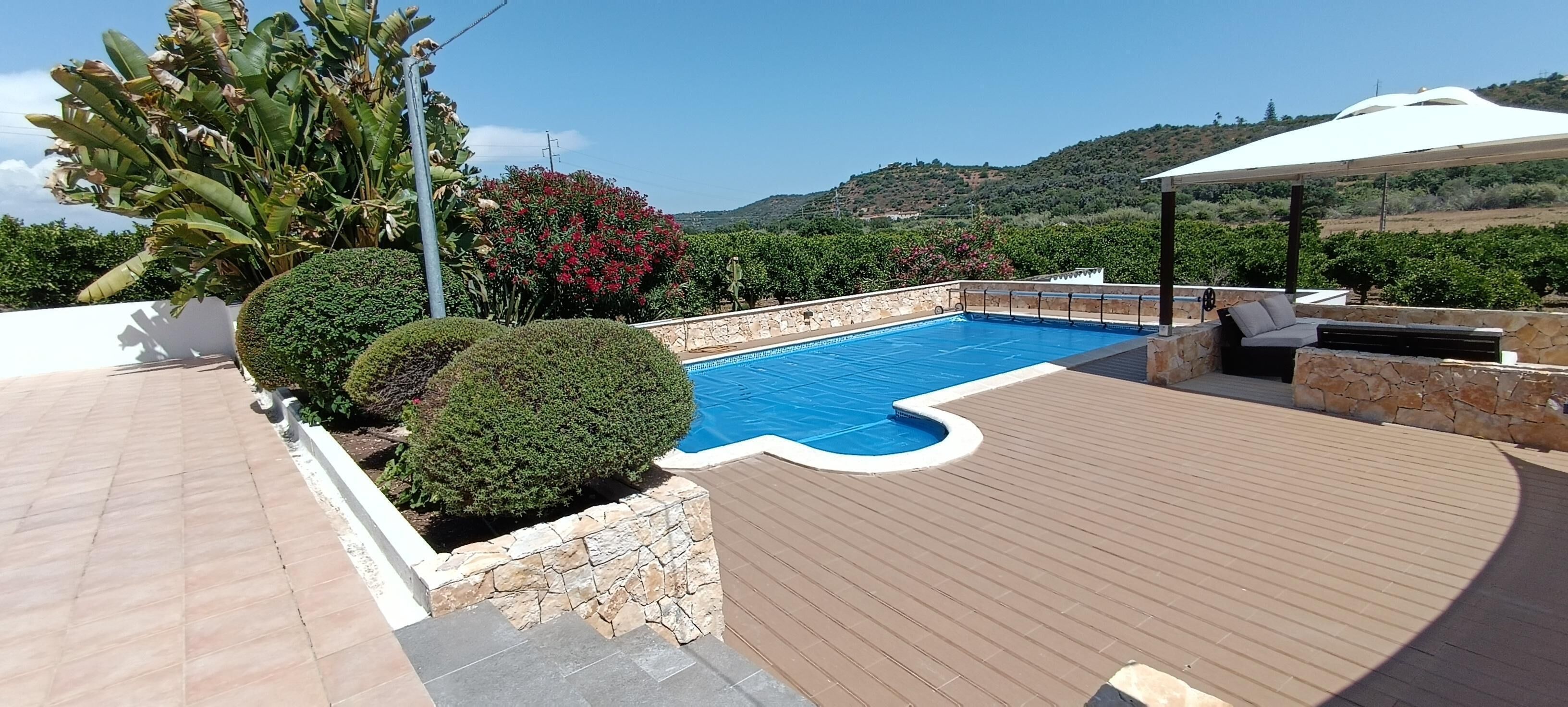 Ein Swimmingpool mit Steinrand, umgeben von einer Holzterrasse und Steinmauern.