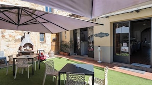 Un pati exterior amb mur de pedra, un forn de pizza i una zona coberta amb taules i caires.