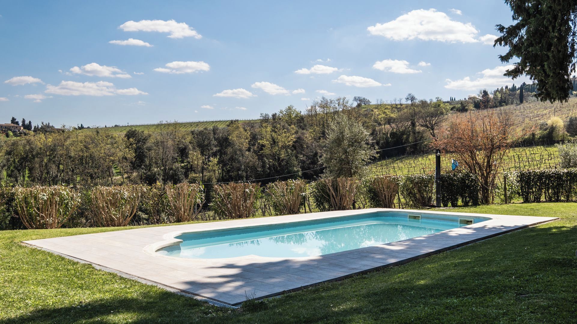 Ein rechteckiger Pool mit gefliestem Sonnendeck, umgeben von einem gepflegten Rasen und einer Kulisse aus Bäumen und Hügeln.