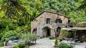 Una casa de pedra amb un camí pedregós que condueix a l'entrada, envoltada de vegetació exuberant i una petita piscina.