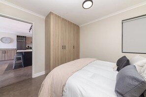 A bedroom with a bed, pillows, a wardrobe, and a view into the kitchen area.