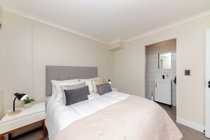 A modern bedroom with a large bed, bedside table, lamp, and a small plant.