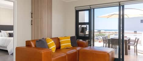 Una sala de estar moderna con un sofá de cuero, un televisor de pantalla plana y un balcón con mobiliario exterior.