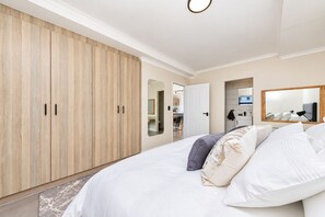 A bedroom with a large wardrobe, a bed with multiple pillows, a mirror, and a view into the bathroom.