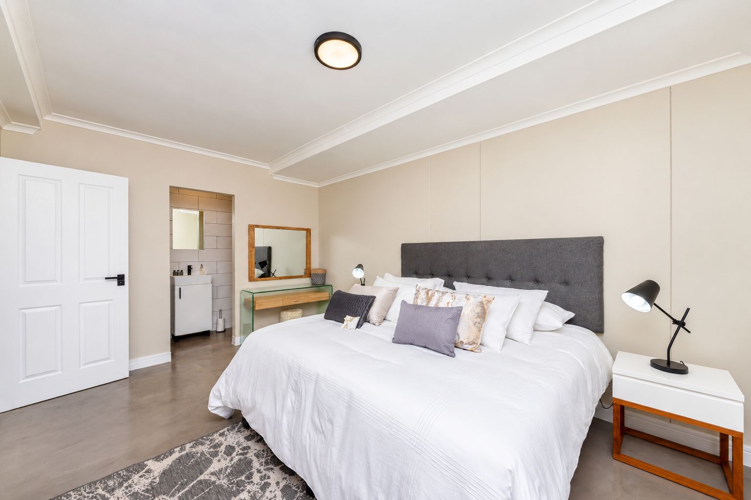 A bedroom with a large bed, bedside tables, a nightstand, a mirror, and a door leading to a bathroom.