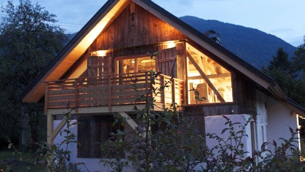 Une cabane en bois dotée d’un balcon, entourée d’arbres et de montagnes.