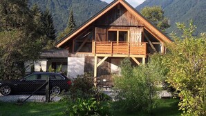 Un chalet en bois doté d’un balcon, entouré d’une végétation luxuriante et de montagnes.