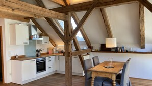 Une cuisine rustique avec des poutres en bois, des armoires blanches et un coin repas comprenant une table et des chaises en bois.