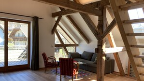 Une pièce avec des poutres en bois, un canapé, un fauteuil et une grande fenêtre.