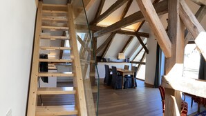 Une pièce de style loft avec des poutres apparentes, une échelle en bois, une table à manger avec des chaises et un tapis à motifs.