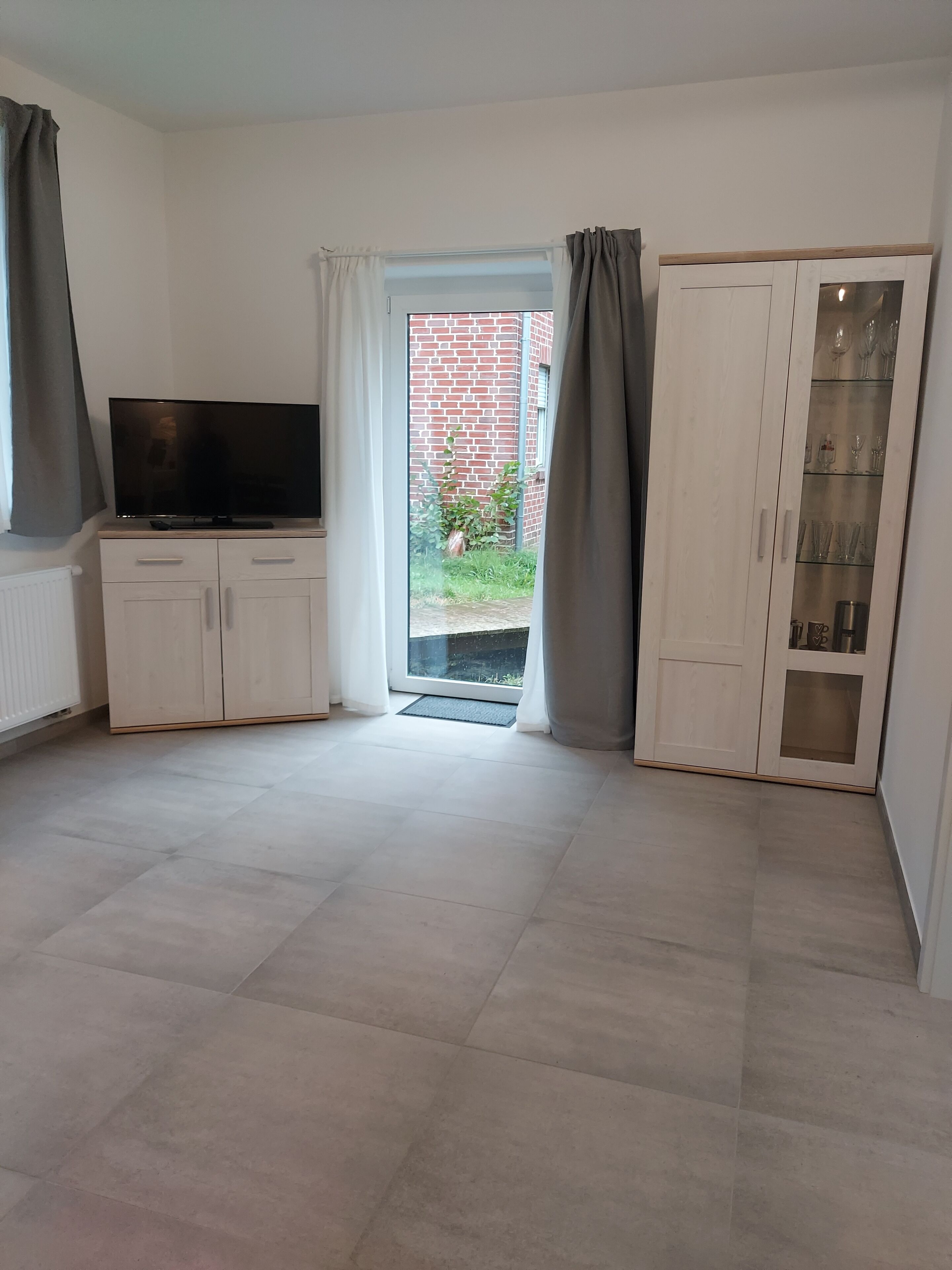 A room with a television on a cabinet, a sliding glass door leading outside, and a cabinet with glass doors.