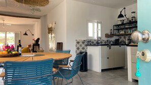 Une cuisine moderne avec des meubles blancs, un plan de travail noir et un panier suspendu. On y trouve également un coin repas avec des chaises bleues et une table en bois.