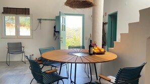 A dining area with a round wooden table, six chairs, a bottle of wine, and a bowl of oranges.