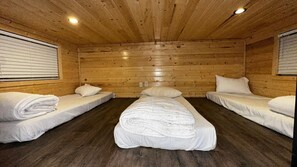 Een blokhut met drie stapelbedden van hout, elk voorzien van wit beddengoed en kussens, en een centraal bed met een witte deken.