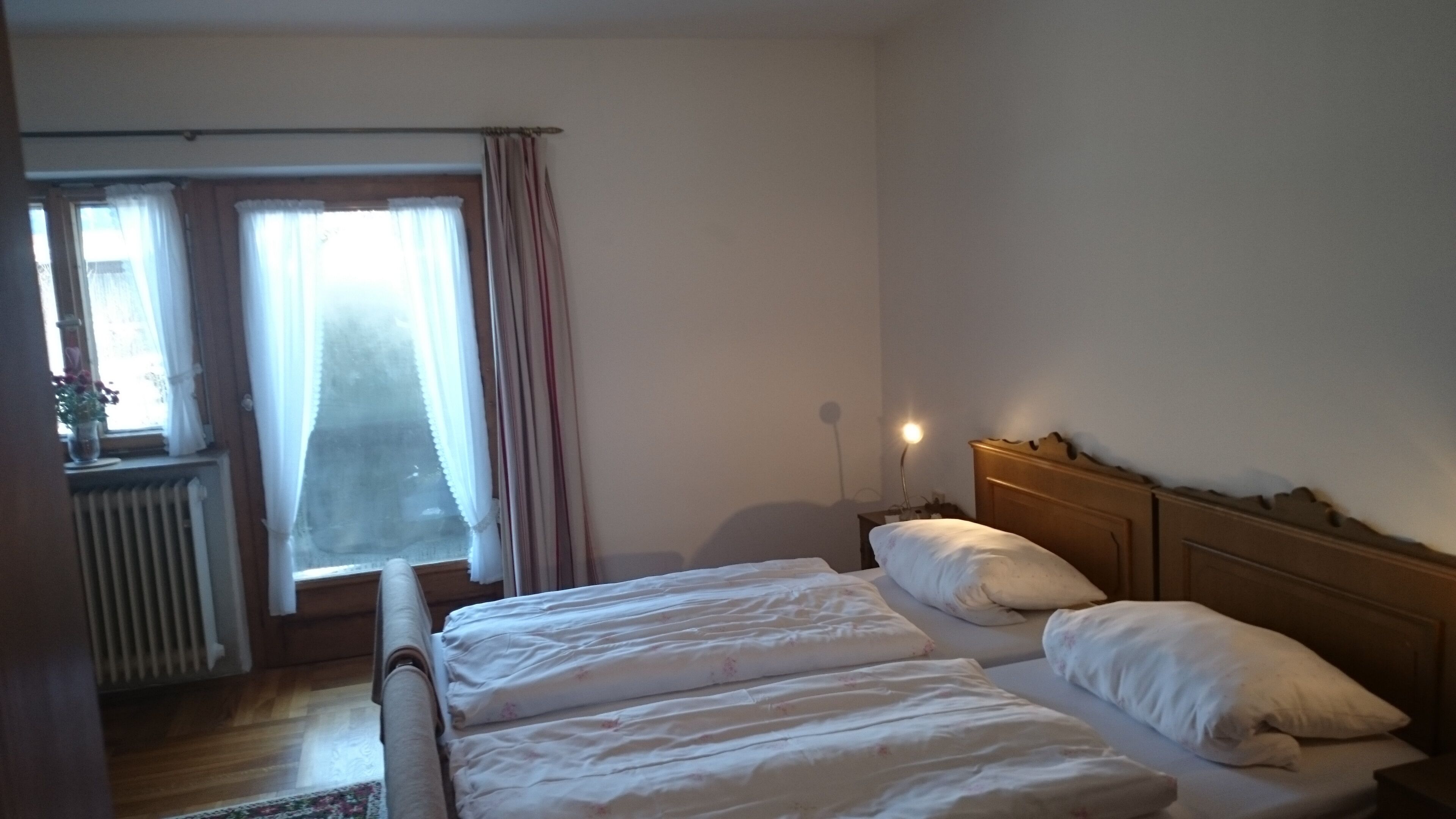 Ein Schlafzimmer mit zwei Betten, einem Fenster mit Vorhängen, einem Heizkörper und einer Nachttischlampe.