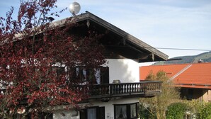 Una casa de dos pisos con un balcón, una antena parabólica y un tejado de tejas rojas.