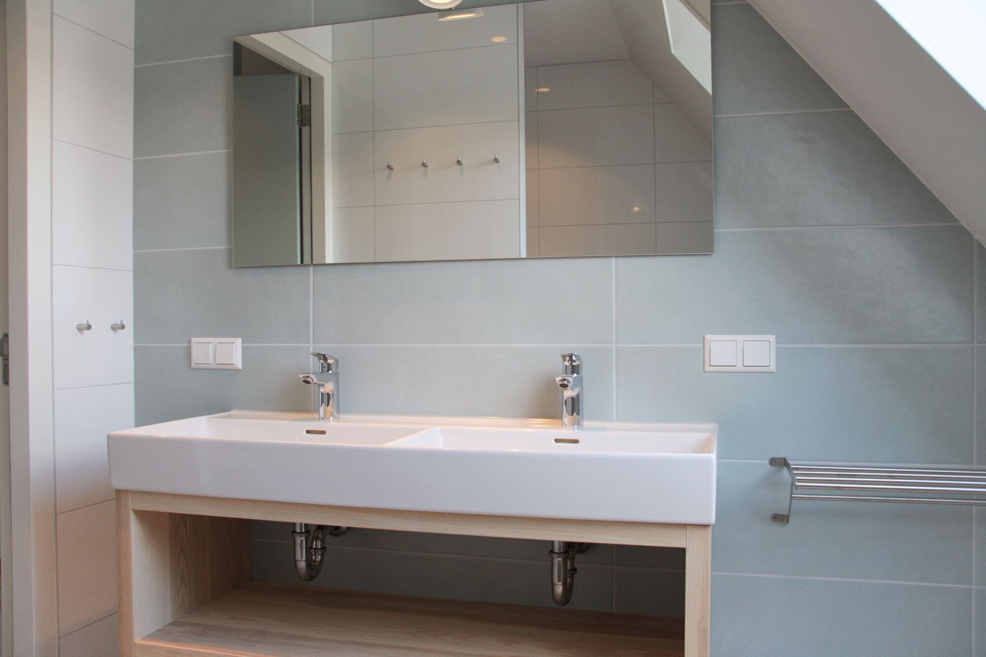 A modern bathroom with two sinks, a large mirror, and a towel rack.