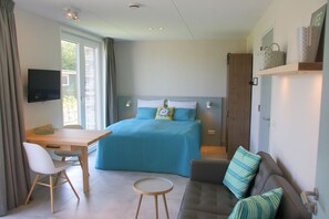 A modern bedroom with a bed, a desk, a chair, a sofa, and a TV.