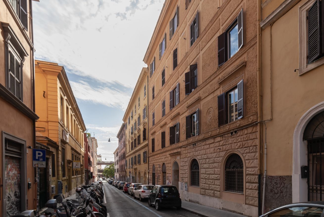 A street lined with parked cars and historic buildings with arched windows and stone facades.