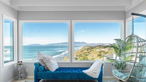 Una stanza con un divano blu, una poltrona sospesa e vista sull'oceano.