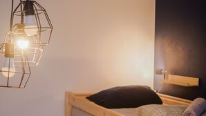 A bunk bed with a wooden frame, a pillow, and a blanket. There is a hanging light fixture above the bed. - Cinnamon Sally Backpackers Hostel (Riga)