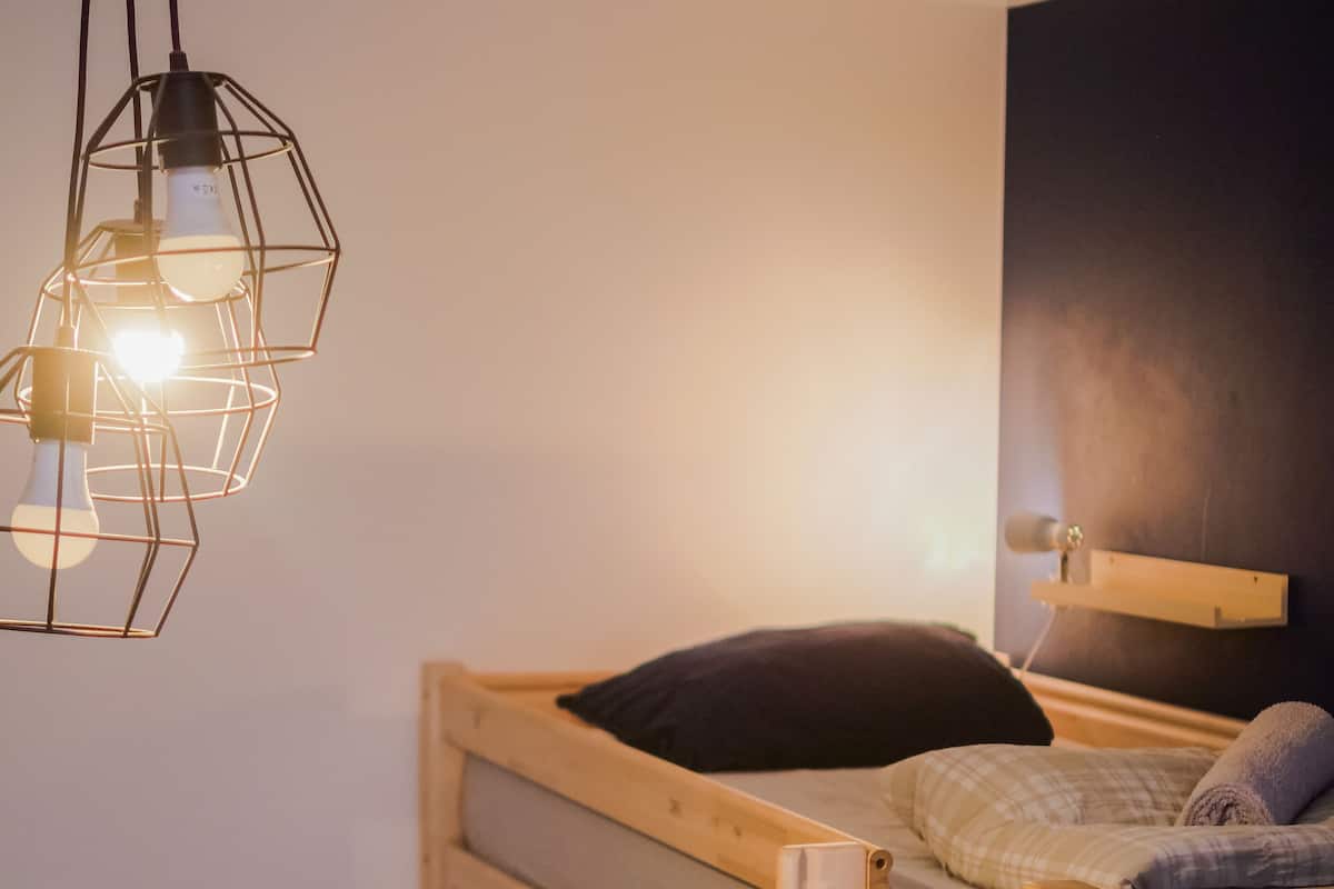 A bunk bed with a wooden frame, a pillow, and a blanket. There is a hanging light fixture above the bed.