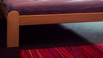 Un dormitorio con cama de madera, ropa de cama púrpura, alfombra roja y negra, y un cuadro en la pared.