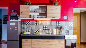 A modern kitchen with a wooden cabinet, a microwave, a refrigerator, and a stove. - Cinnamon Sally Backpackers Hostel (Riga)