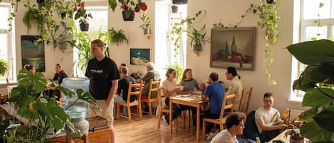A room with wooden flooring, multiple tables, chairs, and hanging plants.