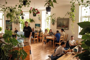 Huoneessa on puulattia, useita pöytiä, tuoleja ja roikkuvia kasveja.