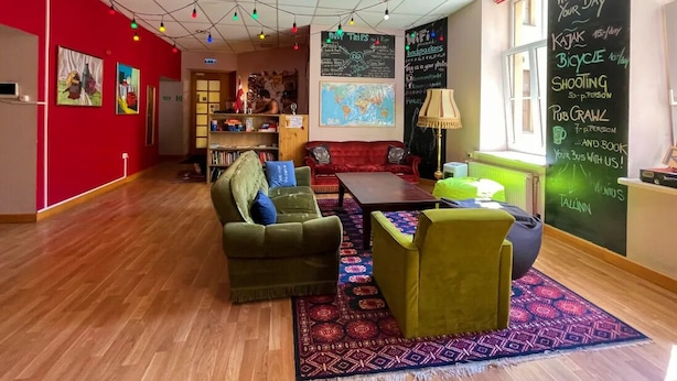 A cozy lounge area with a red wall, a wooden floor, and a seating arrangement including a sofa and chairs. There is a chalkboard with various writings and a map on the wall. - Cinnamon Sally Backpackers Hostel (Riga)