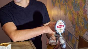 Una persona sirve cerveza de grifo con la etiqueta "CESU Premium" en un vaso. Un cartel indica el precio de la cerveza de barril en 2.90 EUR y el Latvian Balzams en 1.50 EUR.