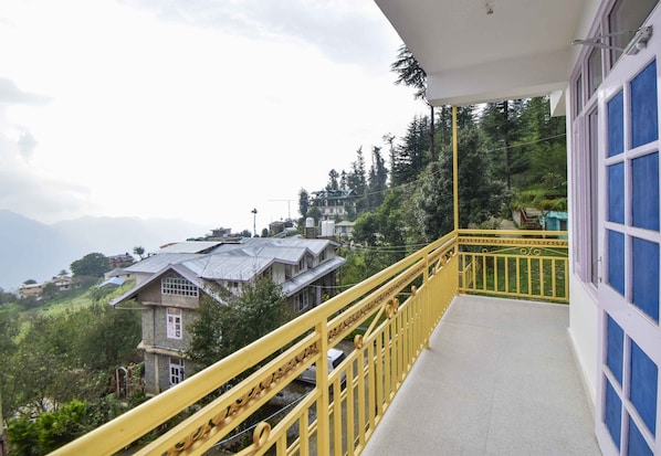 A balcony with a yellow railing overlooking a hillside with houses and trees.