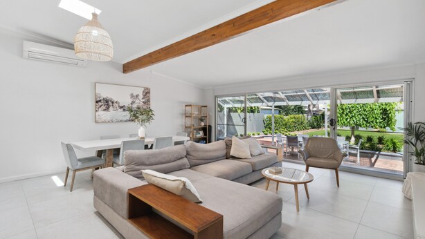 Un salon spacieux avec un grand canapé d’angle, une table basse en bois et un coin repas comprenant une table et des chaises blanches.