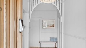 Un couloir avec un banc en bois, une porte dotée d’un détecteur et un tableau encadré accroché au mur.