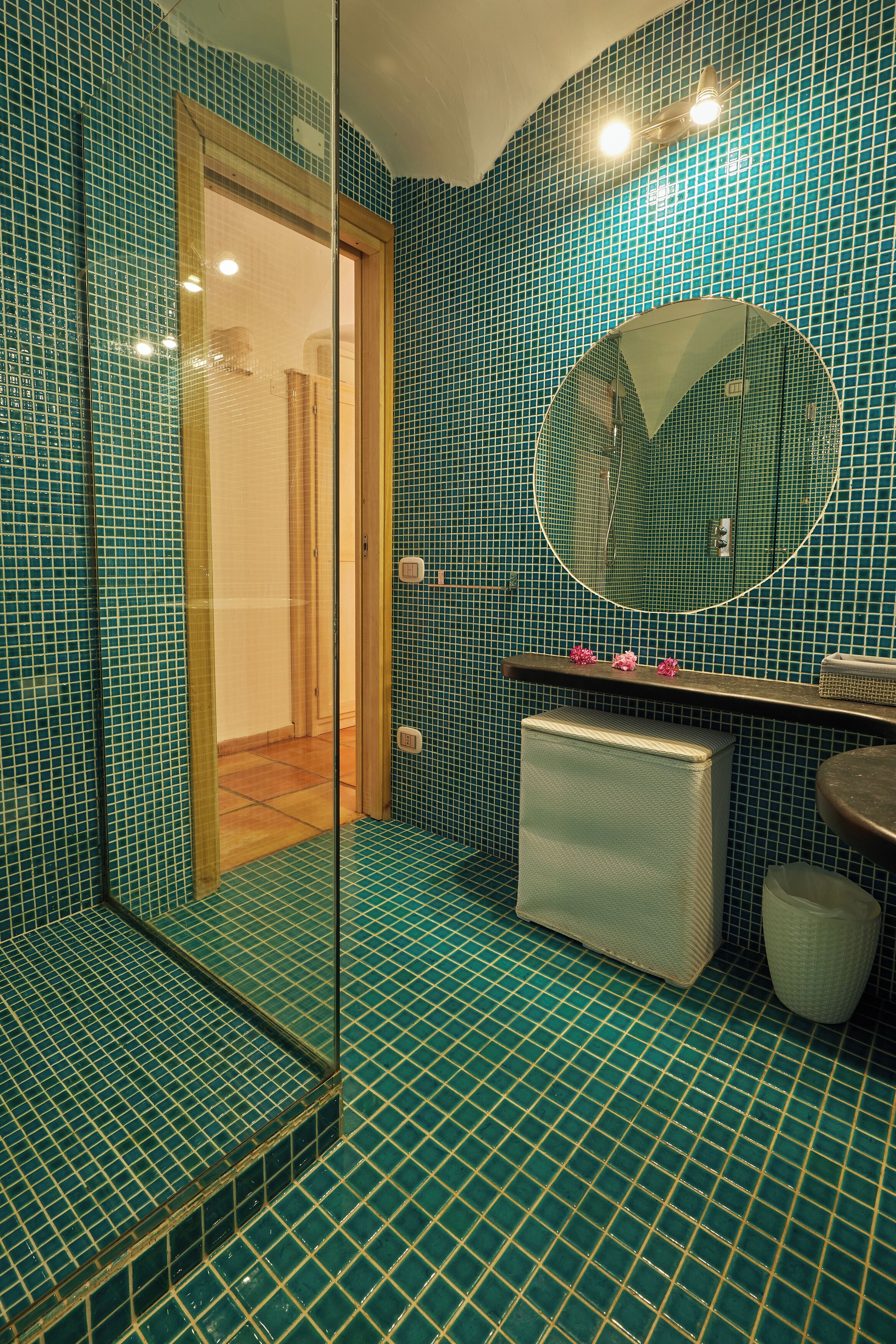 Ein Badezimmer mit Duschkabine aus Glas, einem runden Spiegel und einem Waschbecken mit kleiner Ablagefläche.