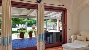 Une pièce dotée d’une porte-fenêtre coulissante donnant sur un patio extérieur avec une piscine, des chaises longues et des plantes en pot.