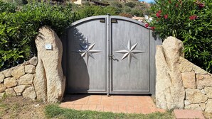 Une entrée fermée par un portail dont le motif est en forme d’étoile, entourée de murs de pierre et de verdure.