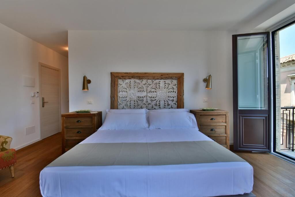 A bedroom with a large bed, wooden nightstands, a decorative headboard, and a view through a glass door.
