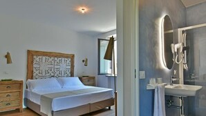 Un dormitorio con cama, mesitas de noche, un espejo y un baño con lavamanos y ducha.