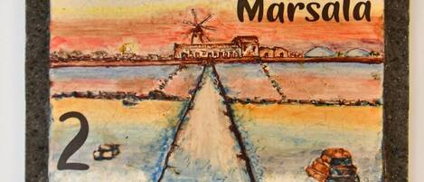 A colorful drawing of Marsala with a windmill, a boat, and a bridge.