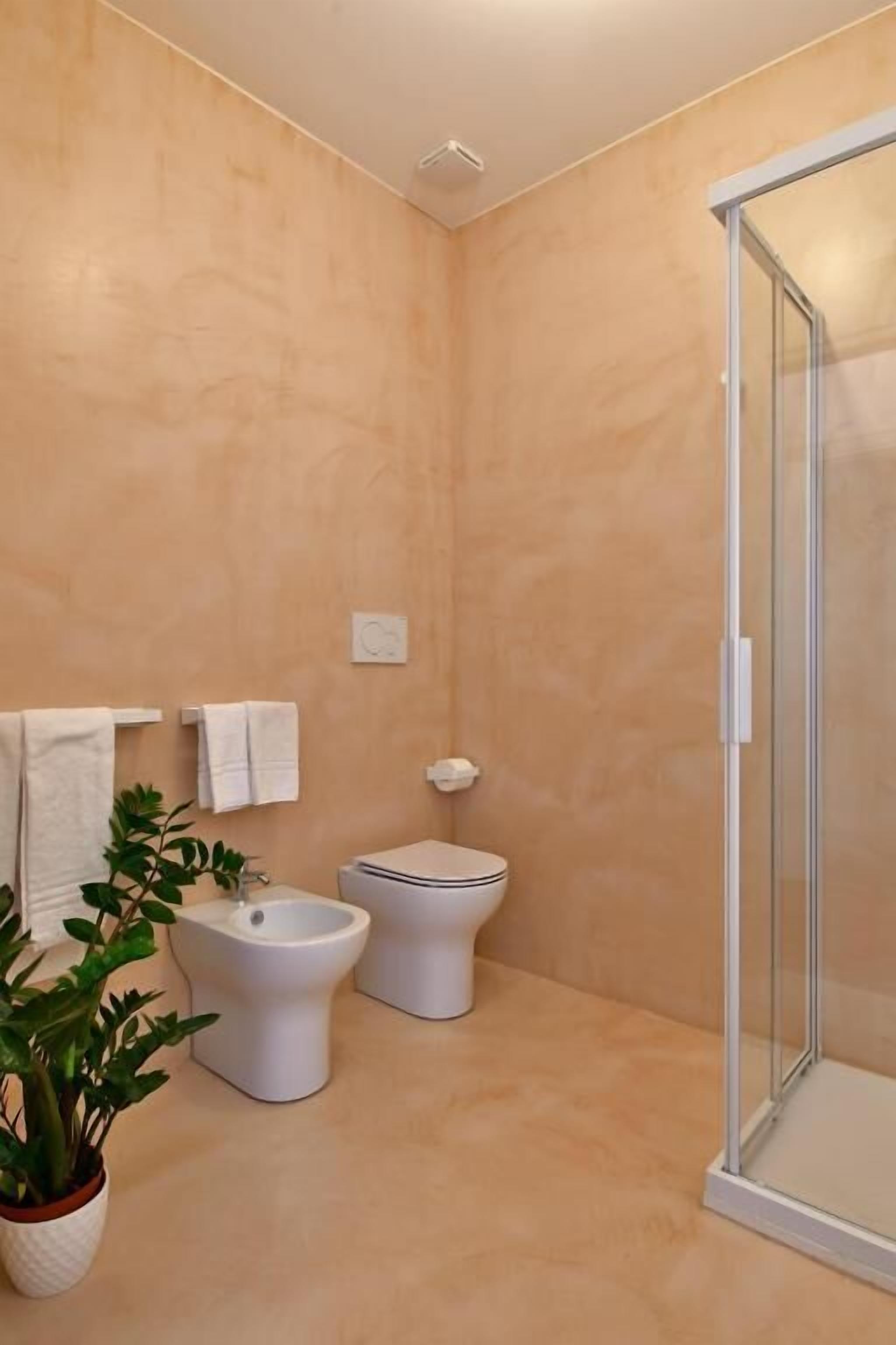 A bathroom with a shower, two toilets, and a potted plant.