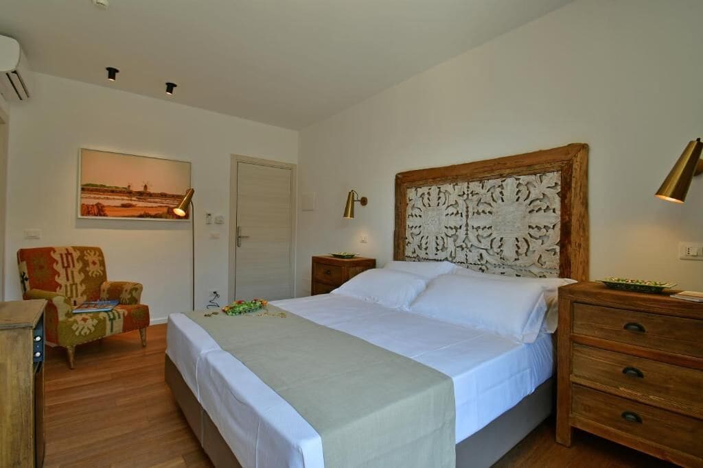 A bedroom with a bed, a chair, a nightstand, and a wall-mounted lamp.