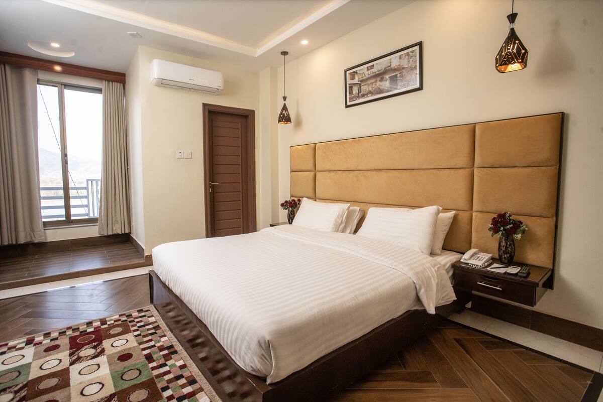 Habitación de hotel con una cama grande, una mesita de noche con un teléfono, una ventana con cortinas y un equipo de aire acondicionado.