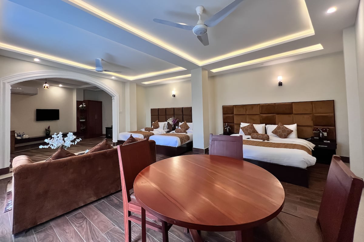 Habitación de hotel con dos camas, una mesa de comedor y un ventilador de techo.