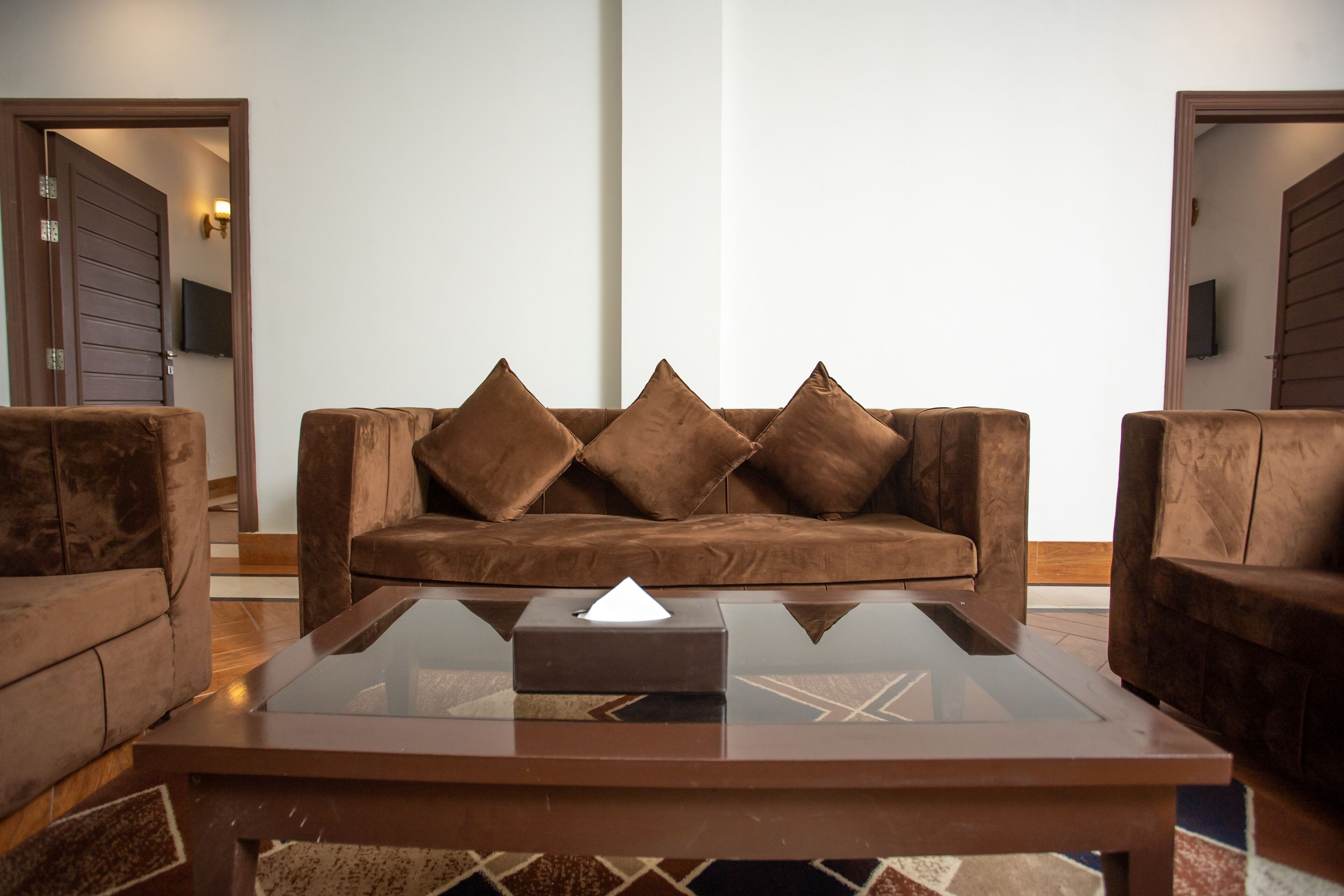 A modern living room with a brown leather sofa, a glass coffee table, and matching armchairs.