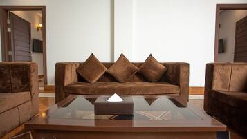 A modern living room with a brown leather sofa, a glass coffee table, and matching armchairs.