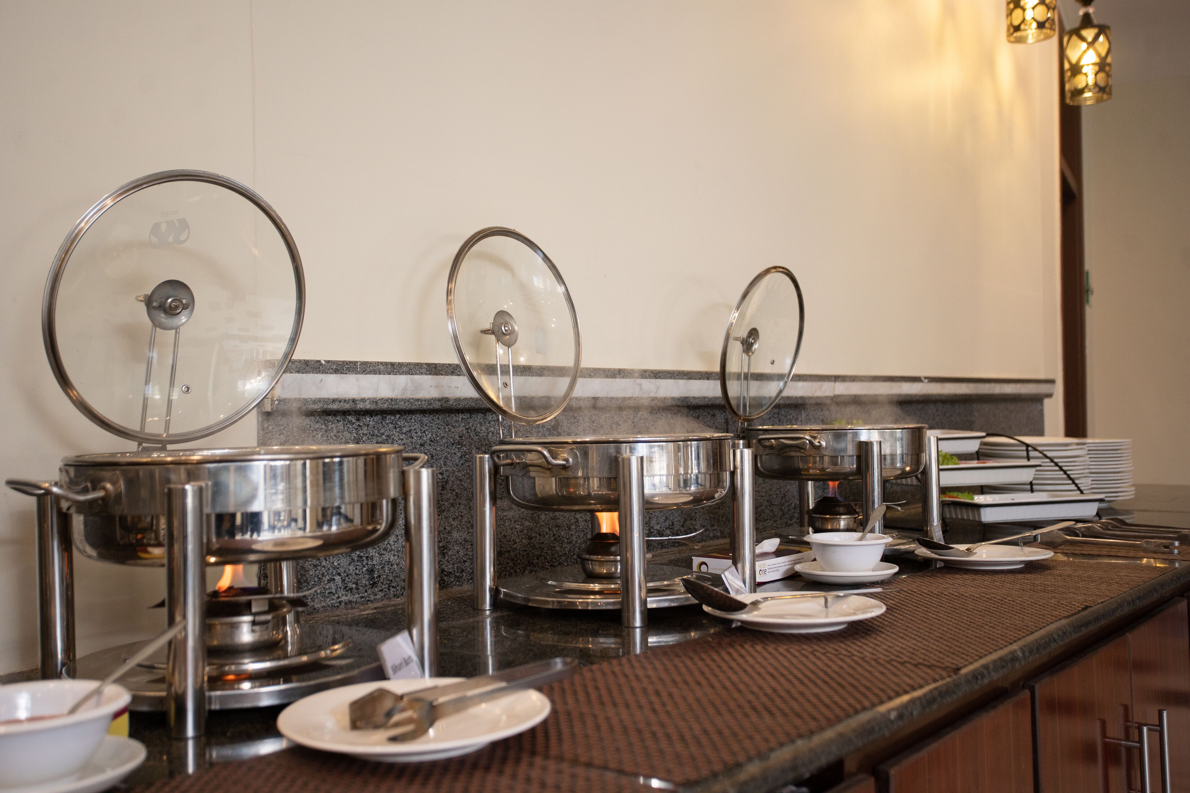 A buffet setup with multiple self-service stations, each with a covered serving dish and a spoon.