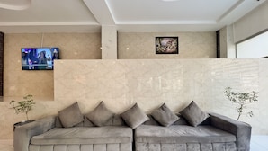 Eine moderne Lobby mit einem grauen Sofa, einem Wandfernseher und einem darüber hängenden Bild.