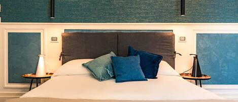 Una cama grande con cabecera oscura, dos mesitas de noche con lámparas y una pared texturizada color verde azulado.